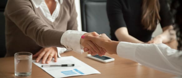 two people shake hands across a desk during a job interview